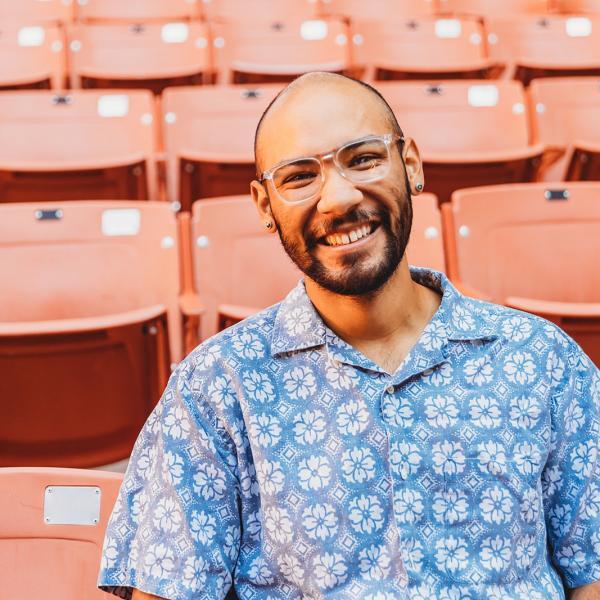 man with glasses and close cropped beard in front of rows of pink stadium chairs