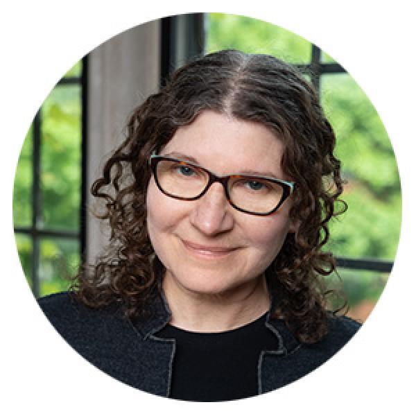 white woman with curly hair and glasses facing forward