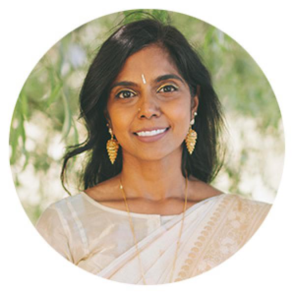 the headshot of a woman of south asian descent with shoulder length hair and a white sari looking at the camera and smiling