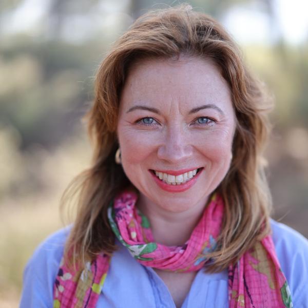 white woman smiling at the camera wearing a pink scarf and light blue shirt